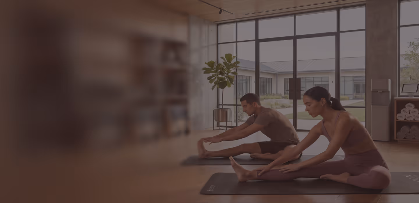 Two colleagues stretching side by side on yoga mats in a bright studio during a corporate wellness session