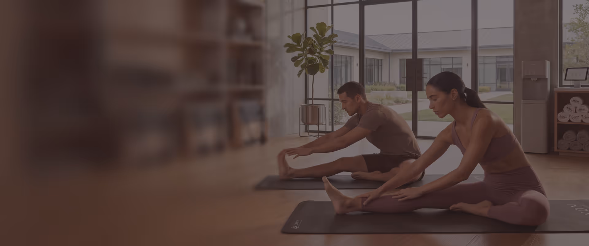 Two colleagues stretching side by side on yoga mats in a bright studio during a corporate wellness session